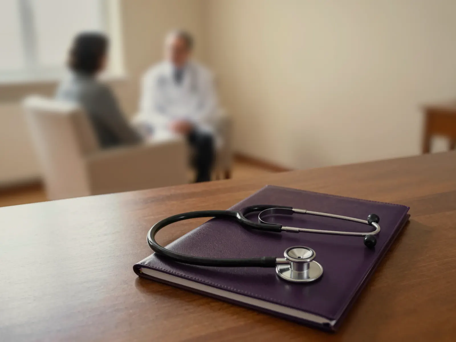 Two people talking in a quiet consulting room, behind a stethoscope resting on a desk.